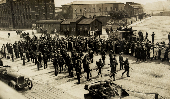 Civil War scene on the quays in Cork; a group of men in
            civilian attire surrounded by armed and uniformed soldiers while 